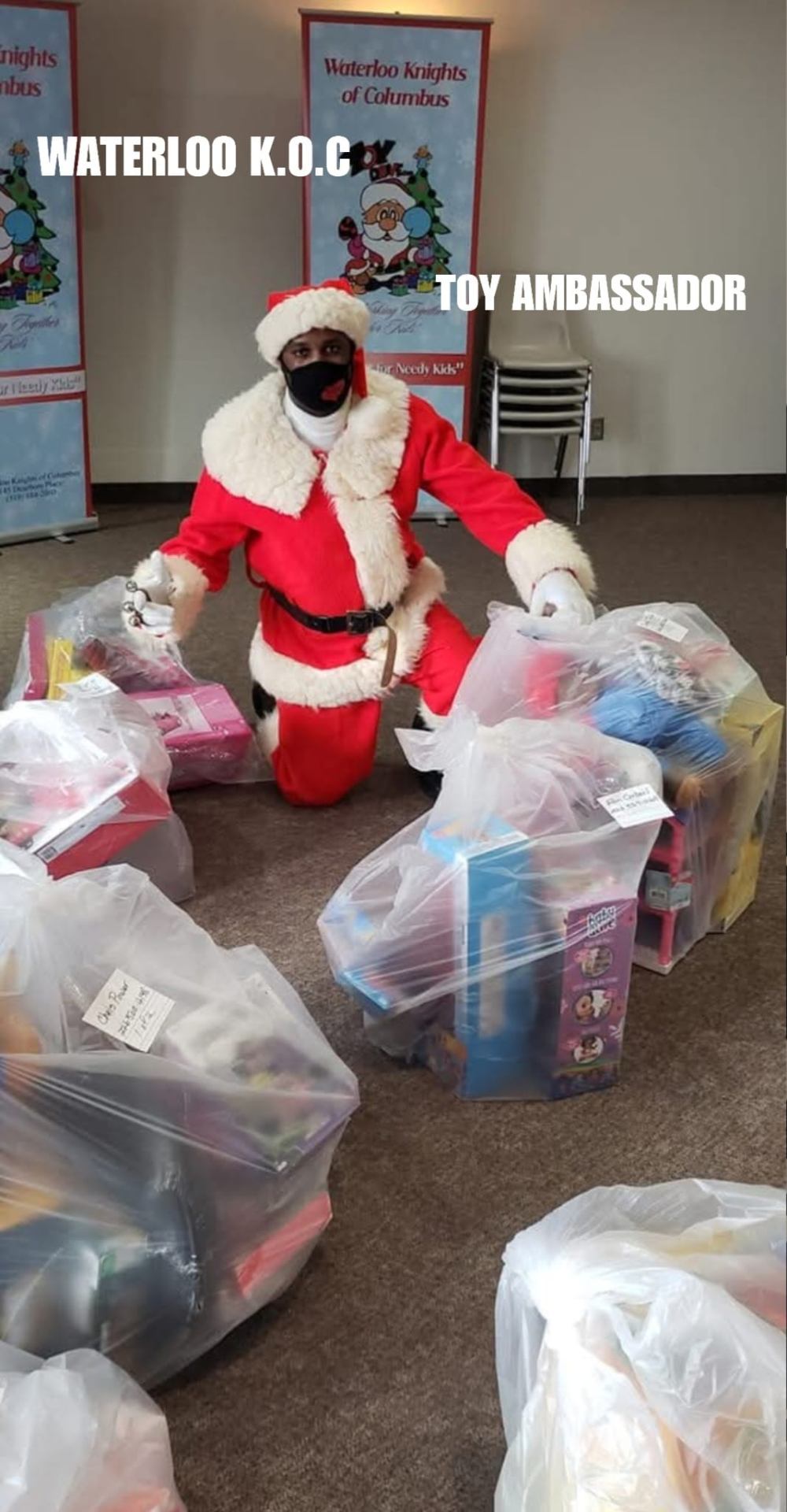 Fitz volunteering as the Toy Ambassador for the Waterloo Knights of Columbus 'New Toys for Needy Kids' campaign, kneeling beside bagged toy donations