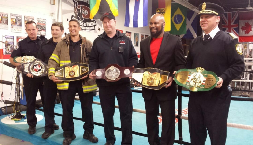 Fitz Vanderpool with Kitchener firefighters and the fire chief, displaying his collection of professional world boxing championship belts at The Whip gym