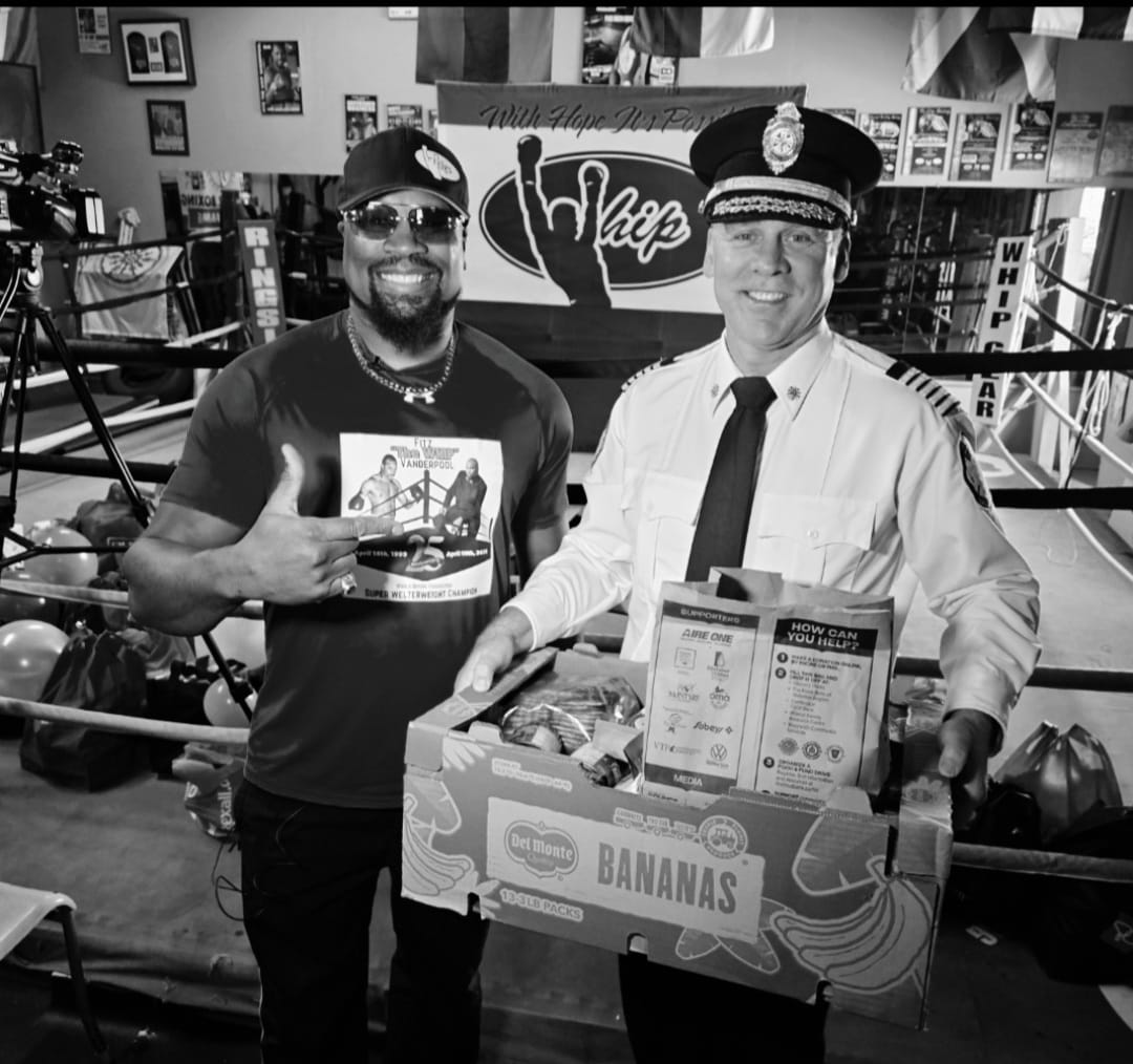 Fitz handing a box of food bank donations to a Kitchener fire services officer at The Whip Boxing Academy