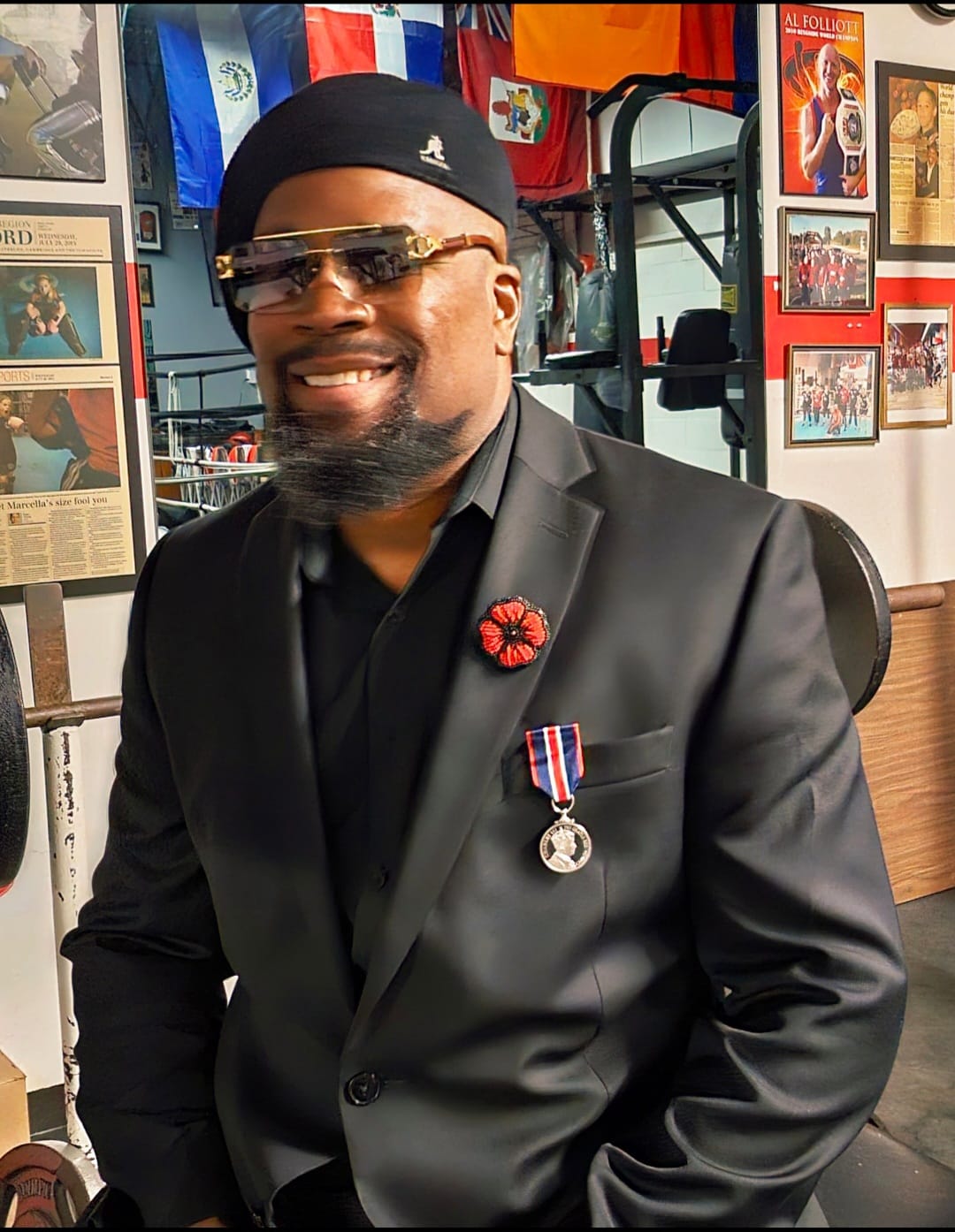 Fitz wearing his King Charles III Coronation Medal and Remembrance Day poppy at The Whip Boxing Academy, surrounded by international flags and championship press clippings