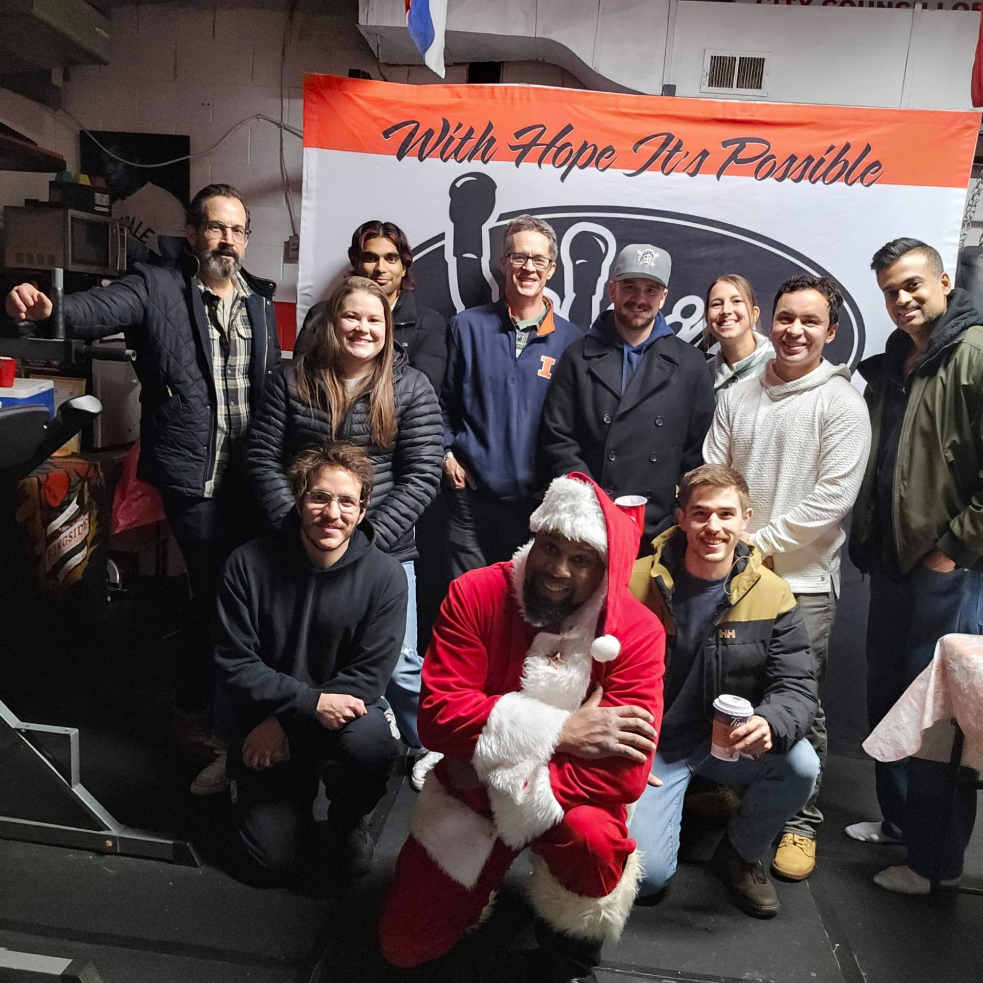 Fitz suited up as Santa with The Whip Boxing Academy members and supporters in front of the gym's 'With Hope It's Possible' banner