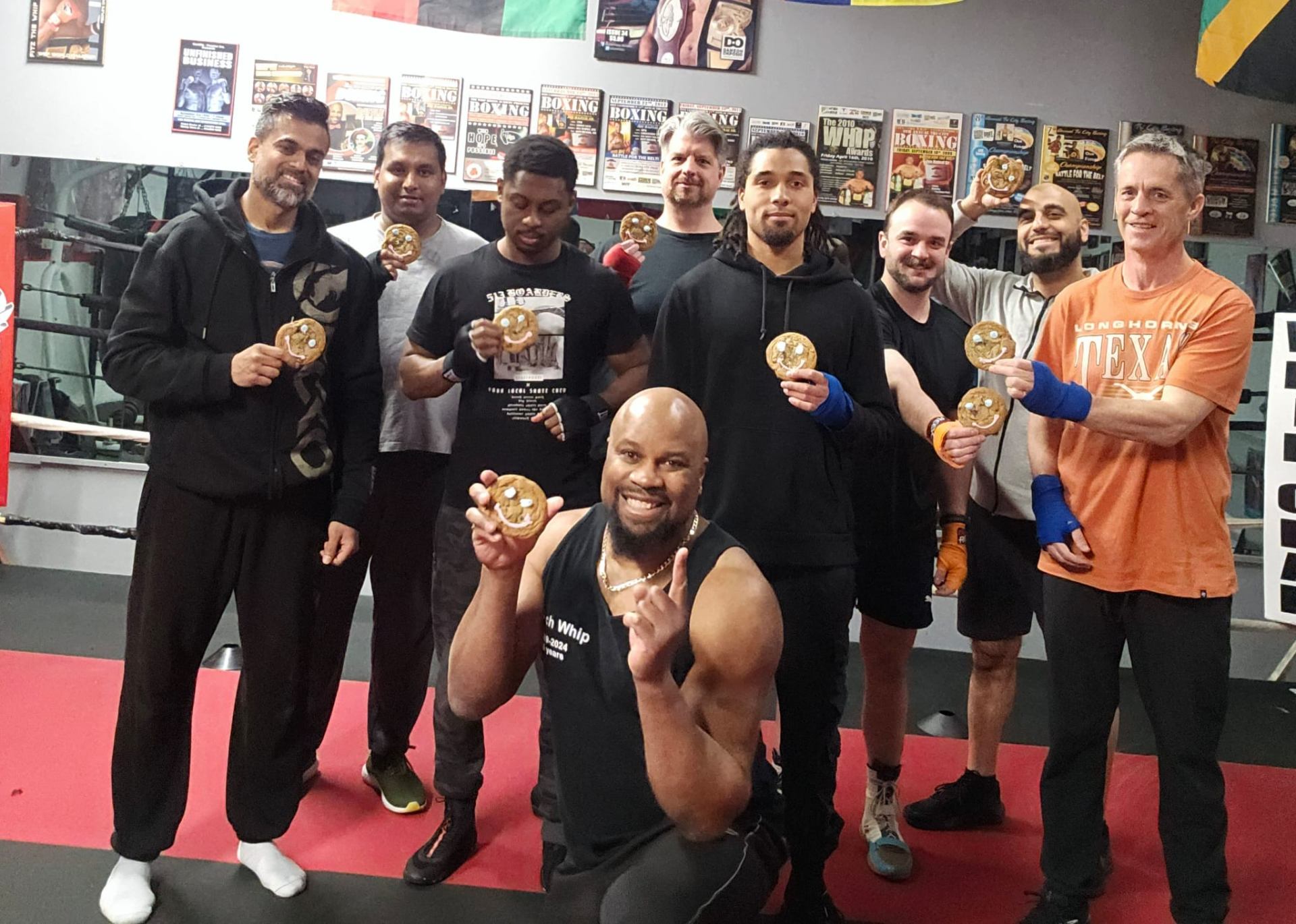 Fitz with The Whip Boxing Academy training group celebrating with smiley-face cookies in front of the gym's wall of championship boxing posters